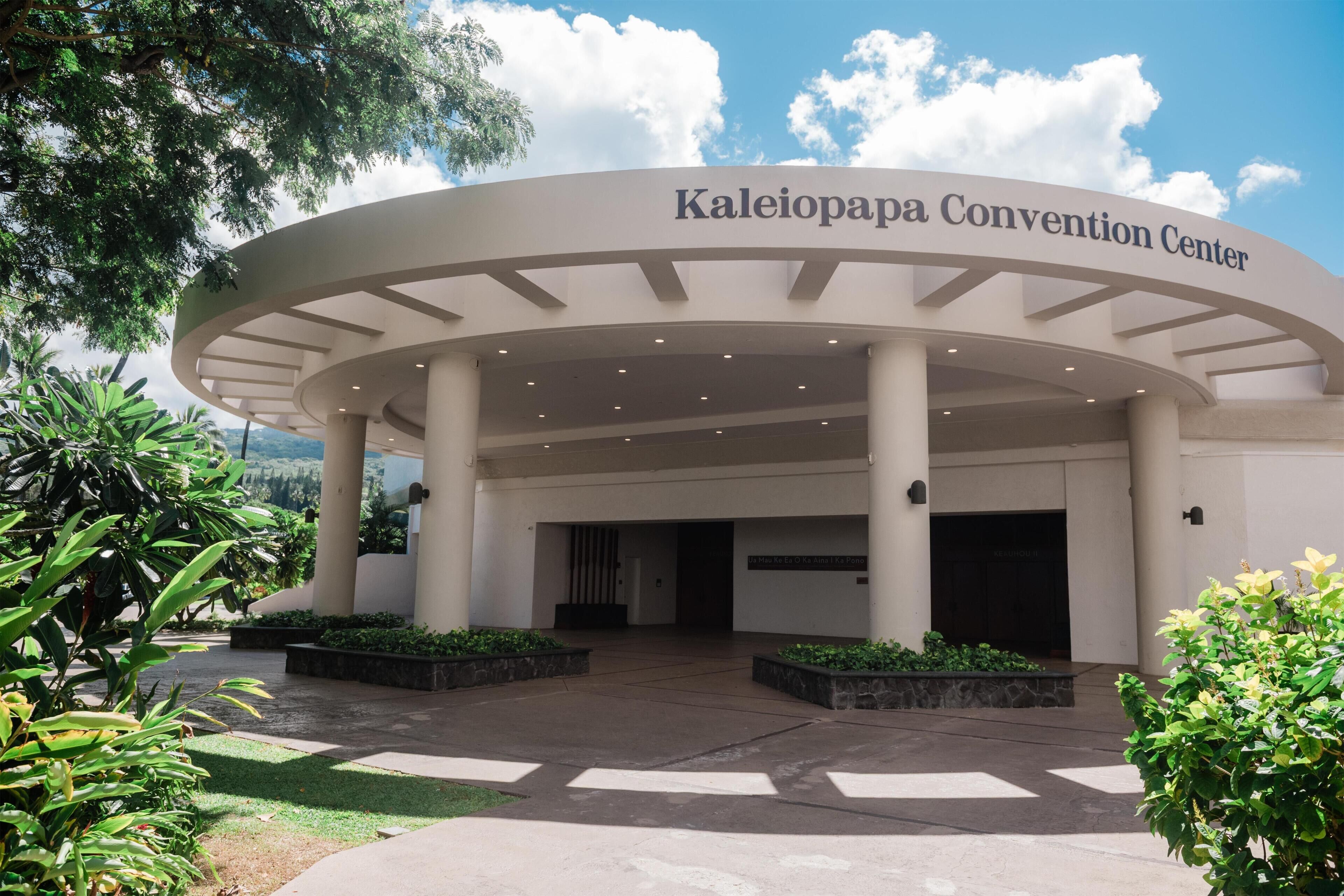 The exterior of the Kaleiopapa Convention Center with a curved entrance, columns, and surrounding greenery.