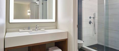 A modern bathroom with a large mirror, a white sink, a glass-enclosed shower, and neatly folded towels on a wooden shelf.