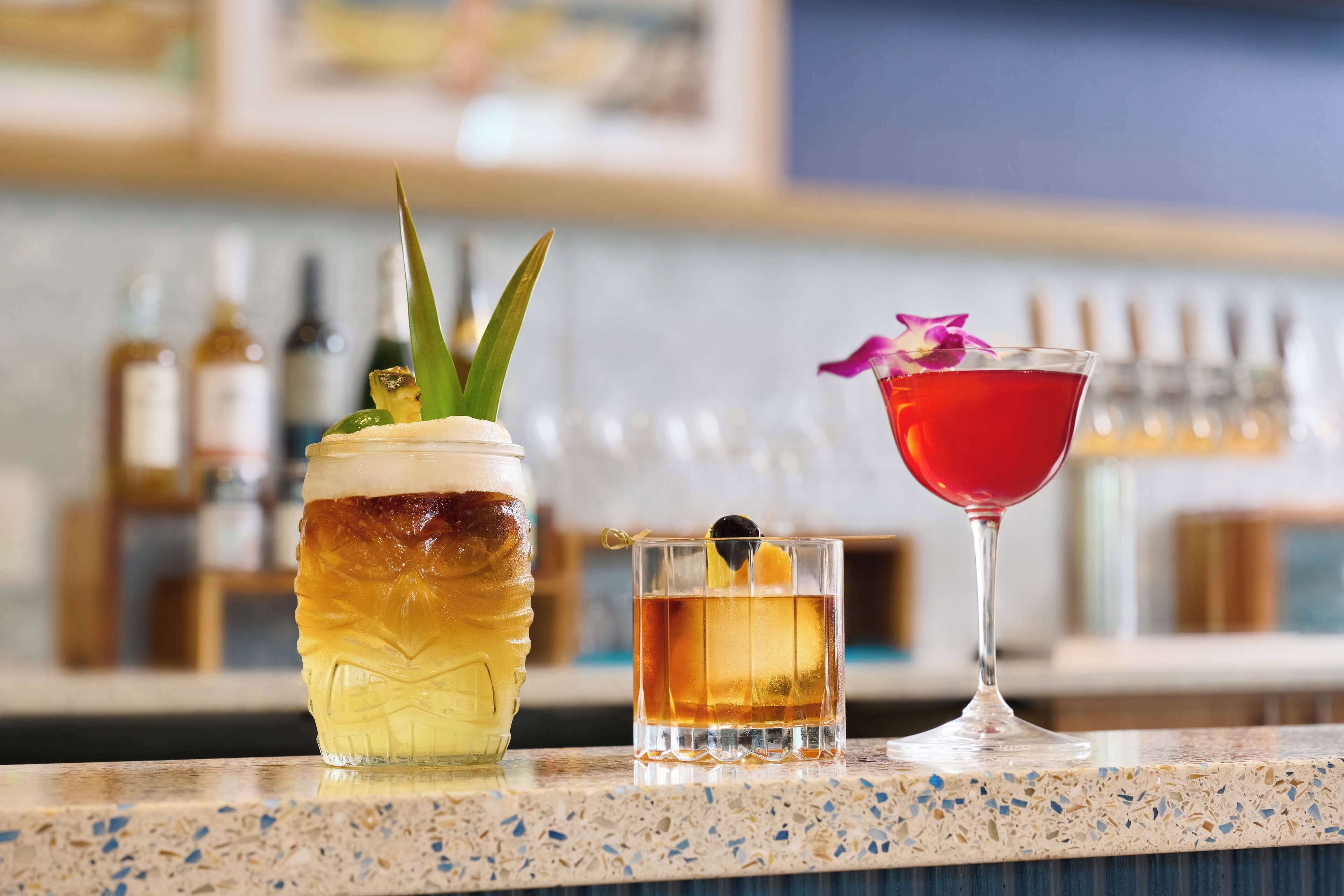 Een bar met diverse drankjes, waaronder een cocktail met bloemen, een glas met citroen en een fles met ananas.