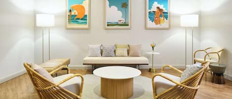 A room with a round coffee table, two wicker chairs, a sofa, and three framed artworks on the wall.
