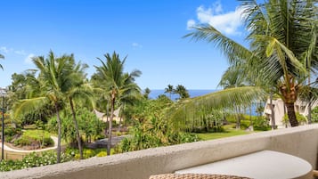 A balcony with wicker furniture, overlooking a tropical garden with palm trees and a clear blue sky.