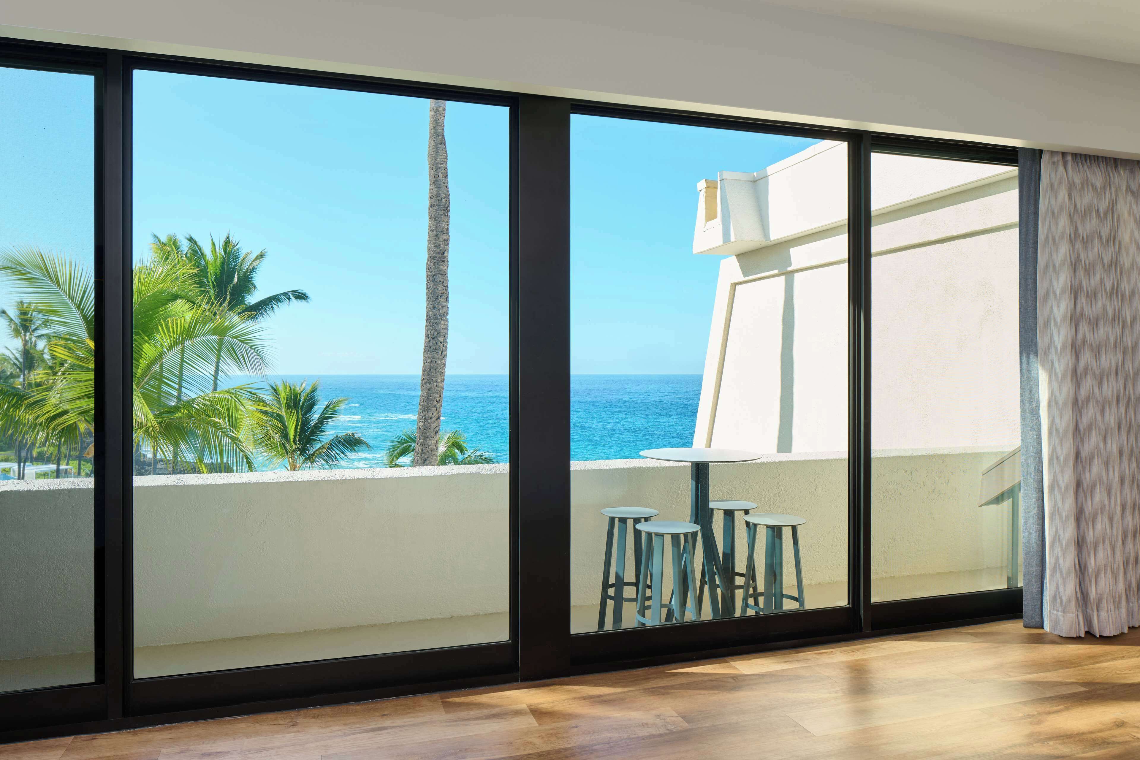 A room with large windows offering a view of the ocean and palm trees.