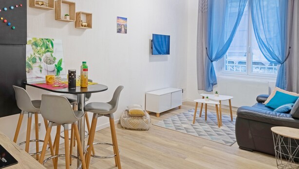 Una sala moderna con sofá, comedor con sillas, una pequeña mesa y área de cocina con refrigerador y armarios.