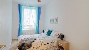 Un dormitorio con cama, mesita de noche, lámpara y ventana con cortinas azules.
