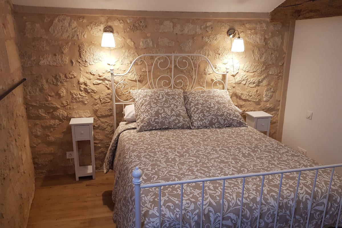 Un dormitorio con pared de piedra, estructura de cama metálica, dos mesitas de noche y una mesilla.