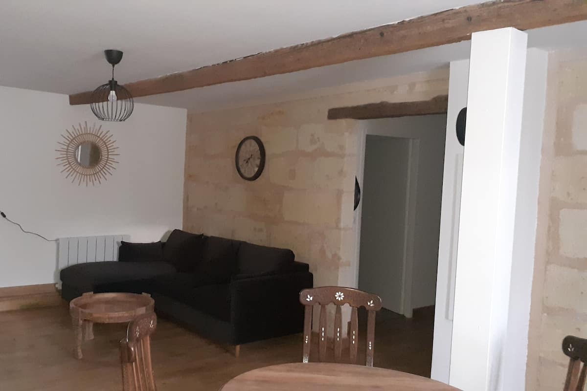 Una sala de estar con un sofá negro, una silla de madera, una mesita, una lámpara de pie y un ventilador de techo.