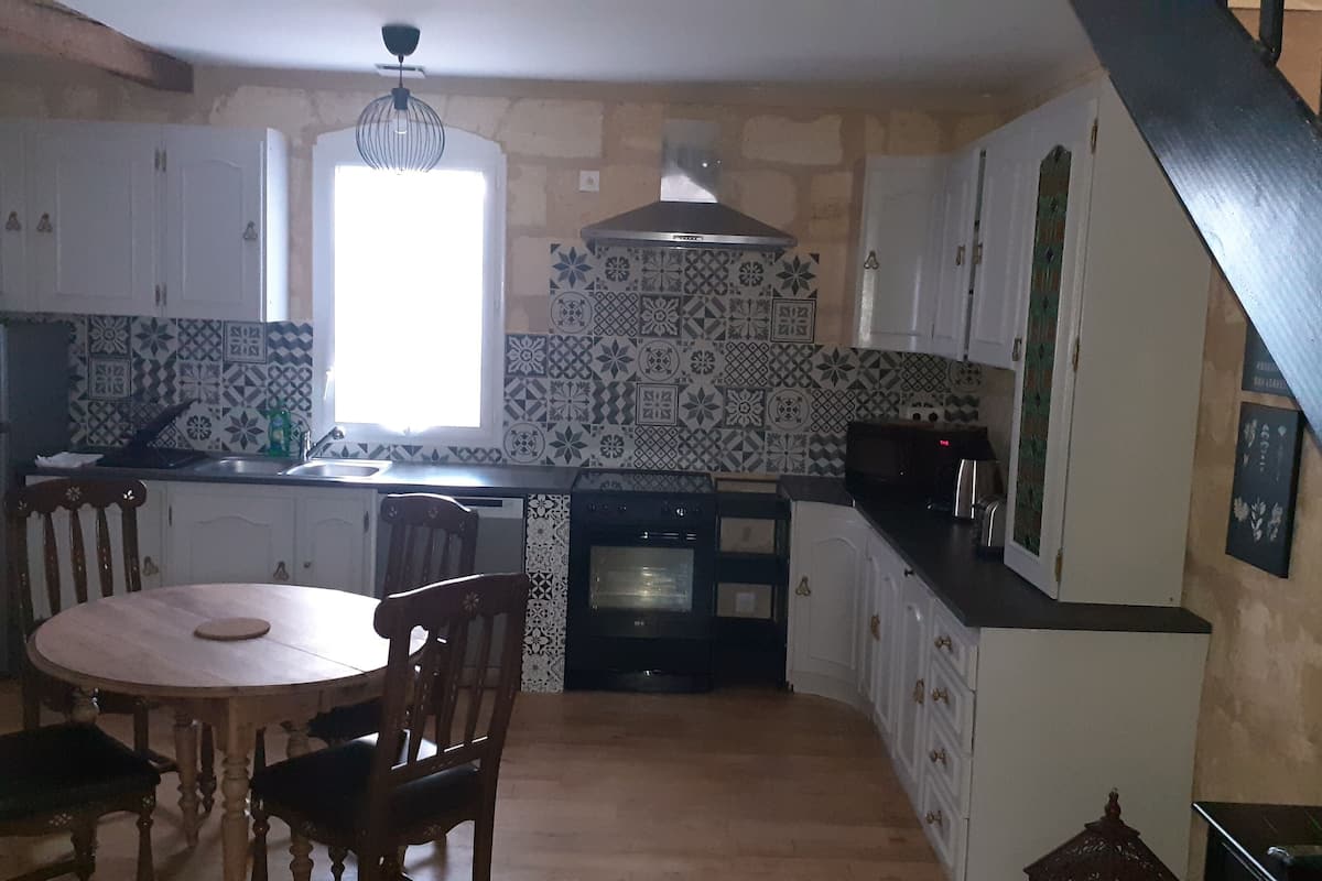 Una cocina con armarios blancos, estufa negra y azulejos decorativos en la pared.