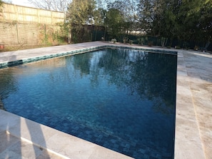 A rectangular swimming pool with a tiled edge, surrounded by a paved deck.