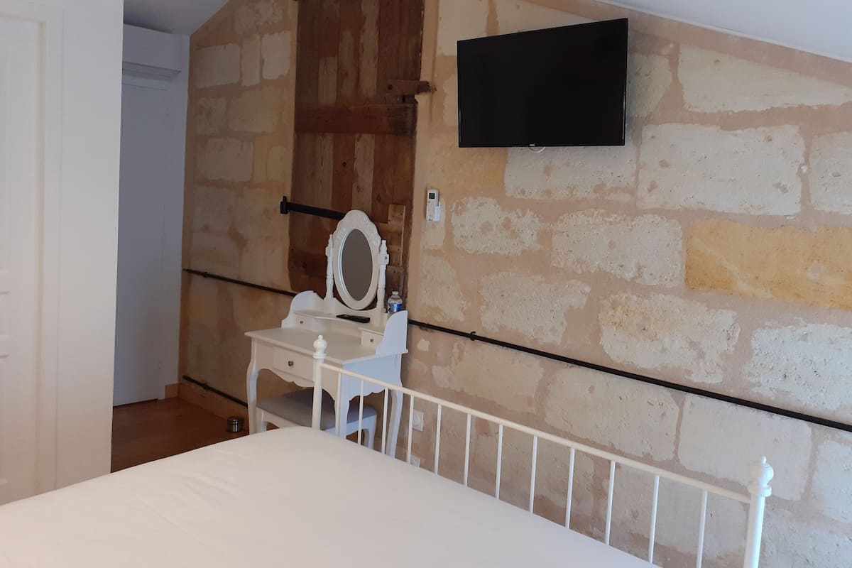 Un dormitorio con cama, cómoda, espejo, televisor montado en la pared y puerta de madera.
