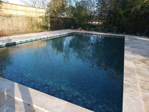 Una piscina rectangular con borde de azulejos, rodeada por una solana pavimentada.