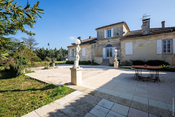 A courtyard with a stone pathway, a statue, a table, and a building with a tiled roof.