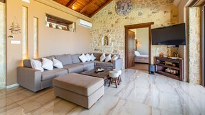A spacious living room with a stone wall, a wooden ceiling, and a large flat-screen TV. - Heated pool + hydro-massage ★ Sea view ★ Near Falasarna (Phalasarna)