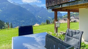 Une table et des chaises en verre dans une pièce offrant une vue sur les montagnes et un village.