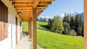 Une structure de pergola en bois, avec un chemin de pierre menant à un bâtiment doté de volets en bois.