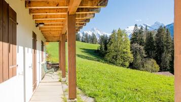 Une structure de pergola en bois, avec un chemin de pierre menant à un bâtiment doté de volets en bois.
