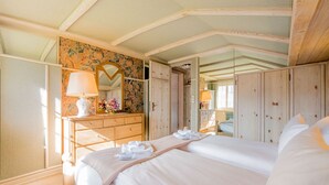 Une chambre avec un grand lit, une armoire en bois et une commode agrémentée d’un miroir et de fleurs.