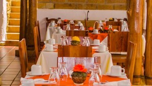 Een restaurant met houten balken, stenen muren en een aan de muur bevestigde televisie. Tafels zijn gedekt met witte tafelkleden en oranje servetten.