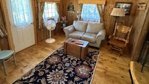 Un interior de cabaña acogedor con paredes de madera, un sofá, una mesita y un ventilador.