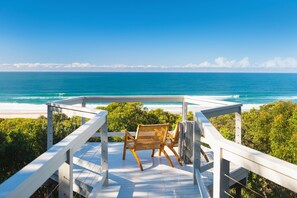 A wooden deck with two wicker chairs overlooking a beach and ocean.