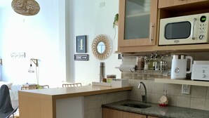 A compact kitchen with wooden cabinets, a microwave, a sink, and a trash can. - Cozy studio in the heart of Recoleta (CABA)