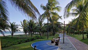 A pathway lined with palm trees leading to a beach, with a bench and a lamp post along the way. - ⭐🌴 House in Guarajuba, 3 Bedrooms with Pool, 150m from the Sea (Guarajuba)