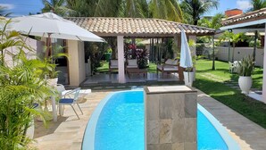 A swimming pool with a pergola and lounge chairs, surrounded by a well-maintained lawn and palm trees. - ⭐🌴 House in Guarajuba, 3 Bedrooms with Pool, 150m from the Sea (Guarajuba)