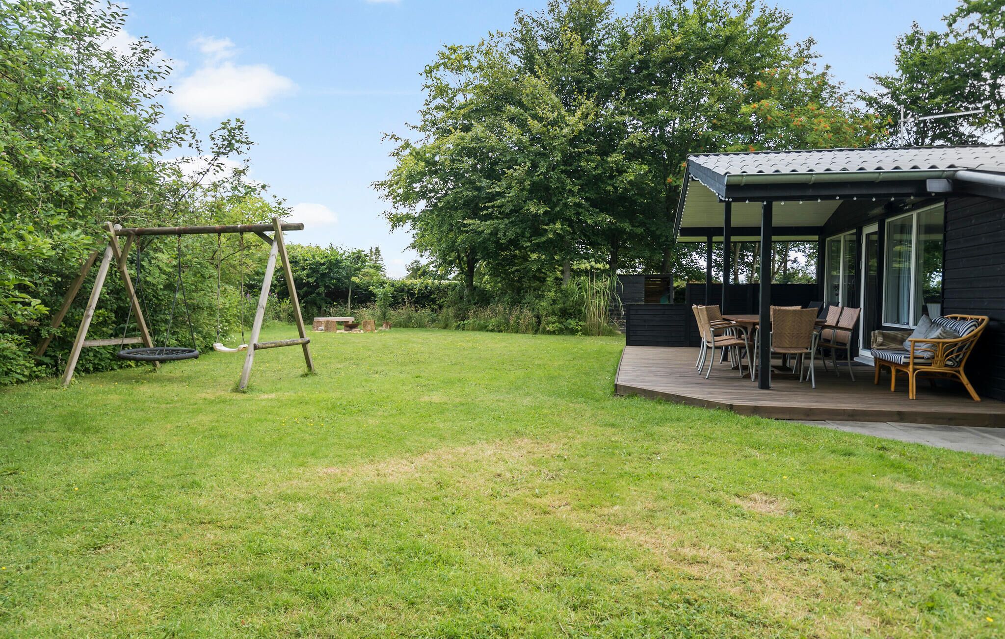A backyard with a swing set, a covered patio with outdoor furniture, and a house with large windows.