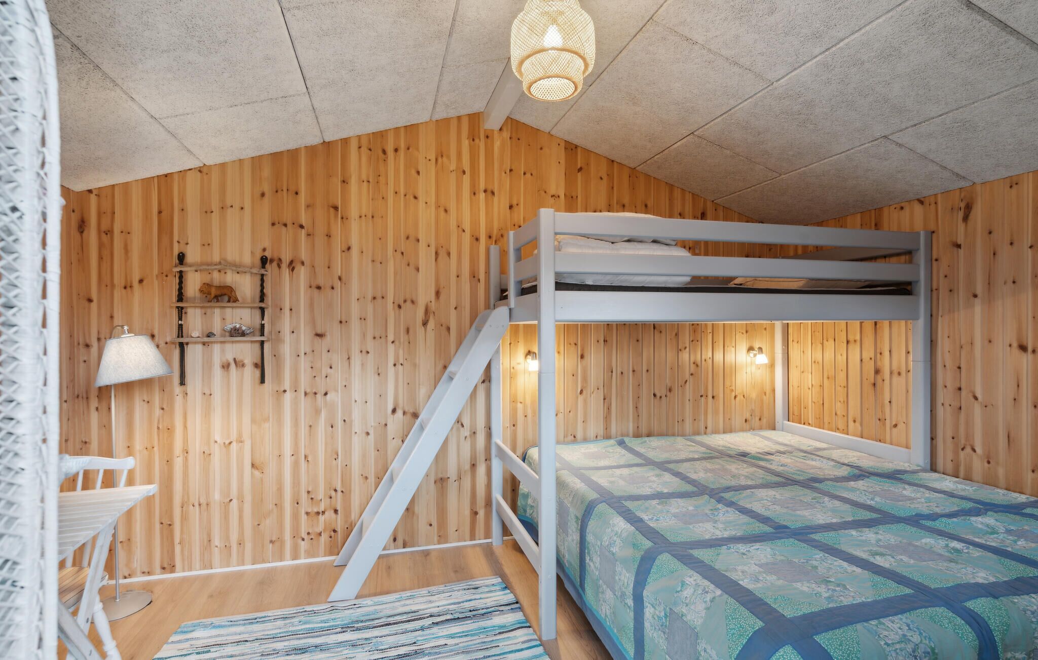 Een slaapkamer met stapelbedden, houten wanden, een hanglamp en een klein plankje met decoratieve objecten.