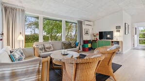 A spacious living room with a sofa, chairs, a coffee table, and a TV. Large windows offer a view of the outdoors. - Amazing home in Hjerm with house a panoramic view (Hjerm)
