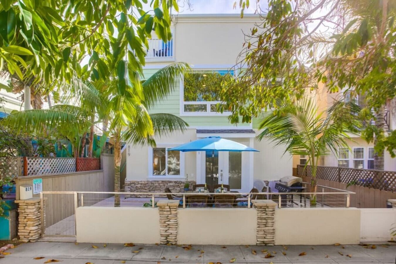 Un edificio de dos pisos con un patio que incluye mobiliario exterior y una sombrilla azul.