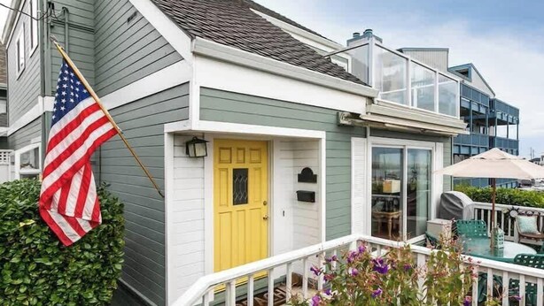 Una casa con puerta amarilla, un balcón con mobiliario exterior y una bandera estadounidense.