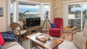 Una sala de estar con televisor, sillón rojo y vista al puerto deportivo.