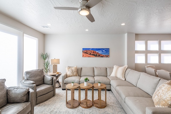 A living room with a beige sofa, two armchairs, a coffee table, and a ceiling fan.