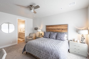 A bedroom with a bed, a nightstand, a chair, a round mirror, and a wooden headboard.