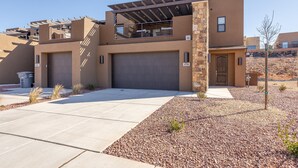 A modern two-story house with a garage, a covered patio, and a small garden area. - Live All In (St. George)