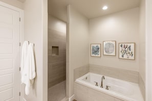 A modern bathroom with a walk-in shower, a bathtub, and three framed artworks on the wall.