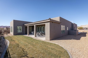 A modern house with a patio, a covered outdoor seating area, and a well-maintained lawn. - Hideaway On The 2nd Green (St. George)