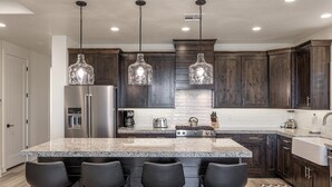 A modern kitchen with dark wood cabinets, a granite island with bar stools, stainless steel appliances, and pendant lighting. - Hideaway On The 2nd Green (St. George)