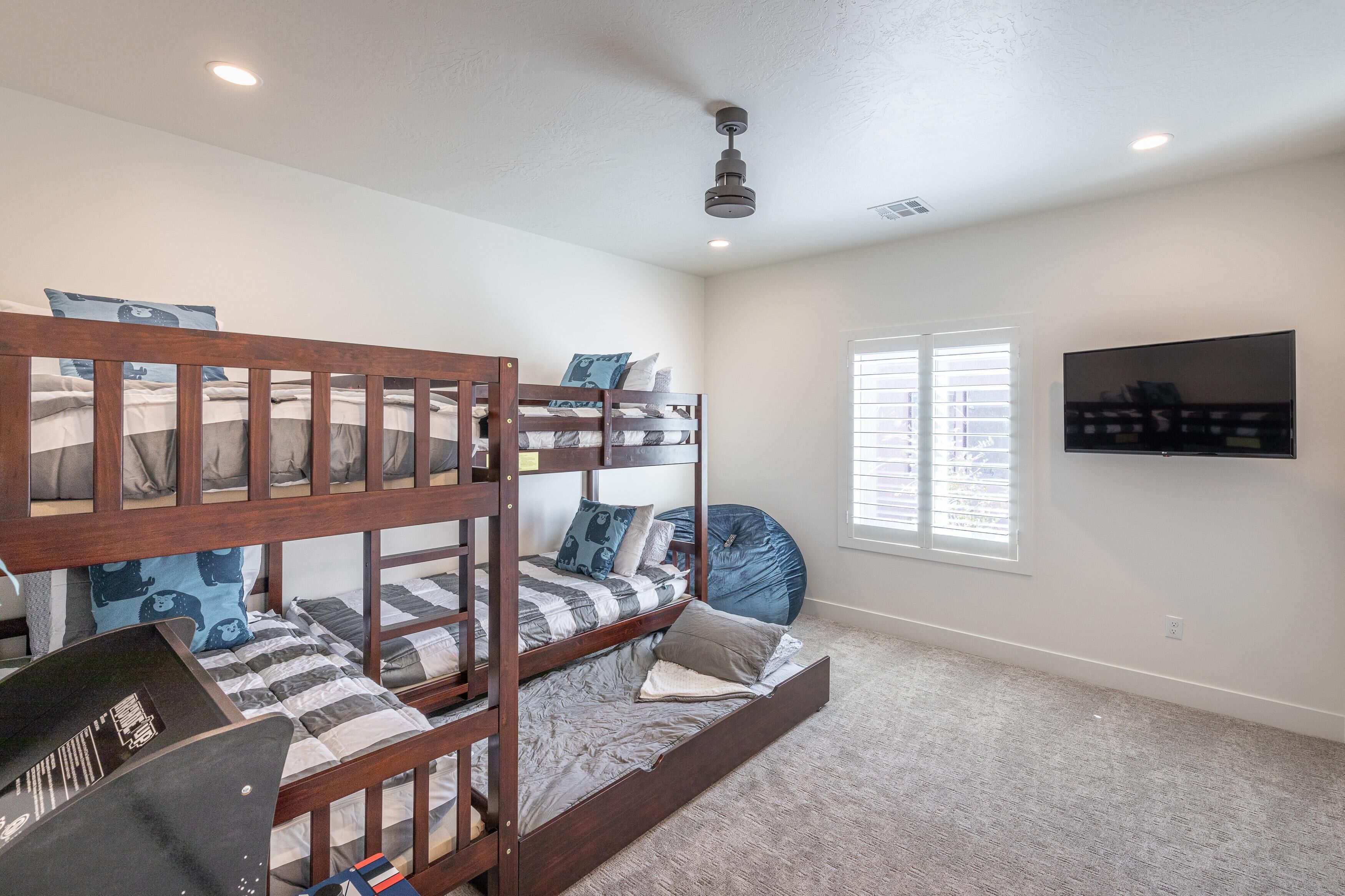 A bunk bed room with a ceiling fan, a mounted TV, and a window with blinds.
