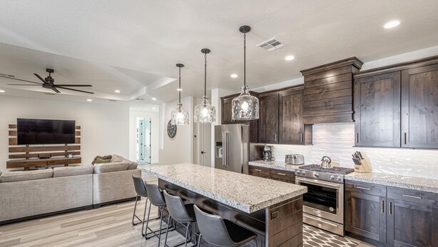 A modern kitchen with dark wood cabinets, granite countertops, and stainless steel appliances. There is a bar area with stools and a large island. - Hideaway On The 2nd Green (St. George)