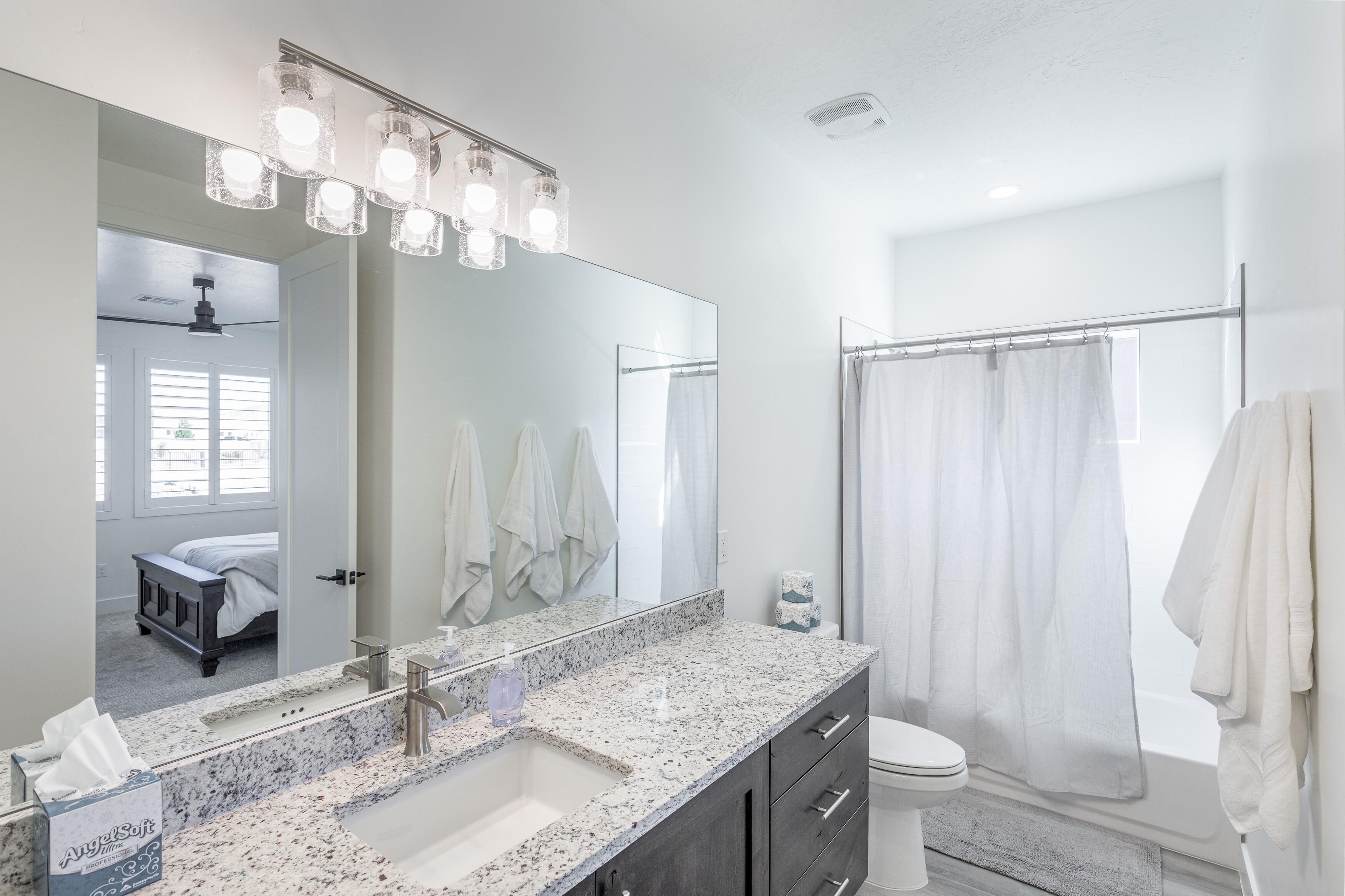 A modern bathroom with a large mirror, granite countertop, and a walk-in shower.