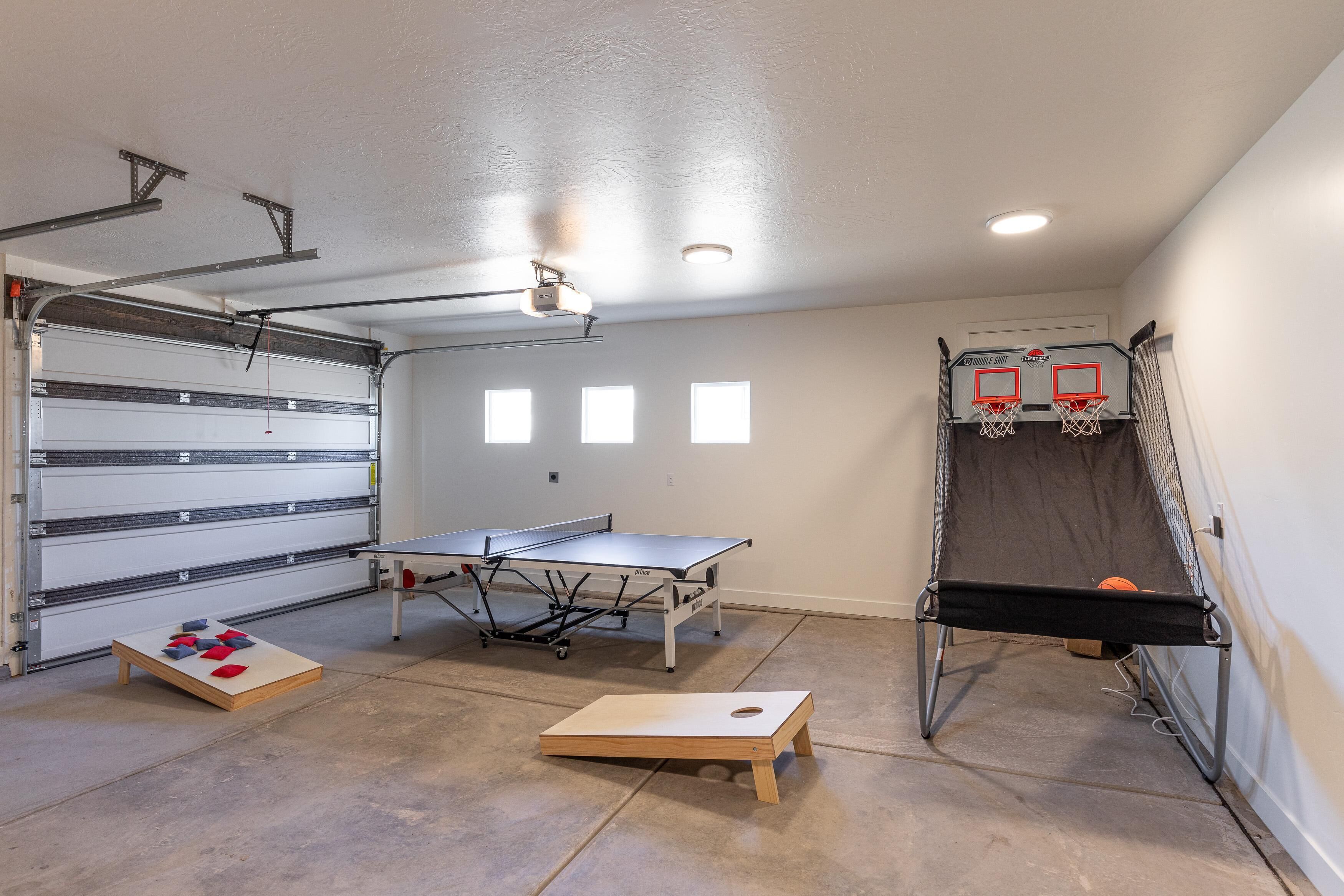 A garage with a ping pong table, a basketball hoop, and a small table with cushions.