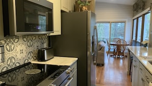 Cozinha moderna com eletrodomésticos de aço inoxidável, painel decorativo atrás do fogão e área de jantar com vista.