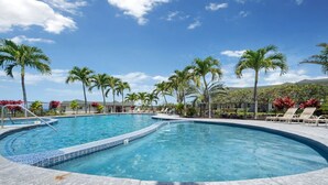 A large, clear swimming pool with multiple lanes, surrounded by palm trees and lounge chairs.