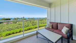 A balcony with a sofa and a table, overlooking a lush landscape and the ocean.