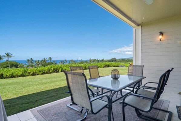 Une terrasse extérieure avec une table et des chaises, offrant une vue sur un paysage verdoyant et luxuriant ainsi que sur l’océan.