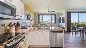 A modern kitchen with a stove, oven, and dishwasher, large windows with a view of the ocean, and a dining area with a table and chairs.