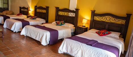 A hotel room with four beds arranged in a row, each with a wooden headboard and white bedding.
