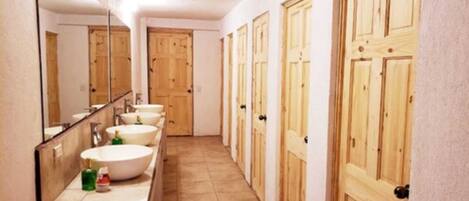 A long hallway with a row of sinks and mirrors, wooden doors, and a tiled floor.