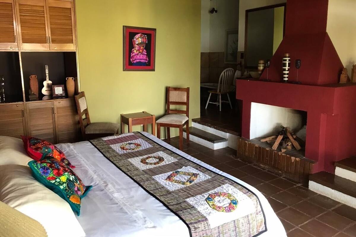 Een gezellige kamer met een bed, een sprei, een open haard en een houten kast.